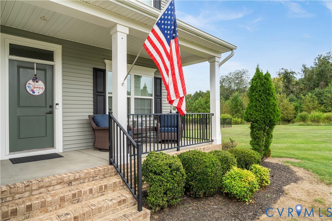 Covered front porch with white columns, brick stairs, and black railings