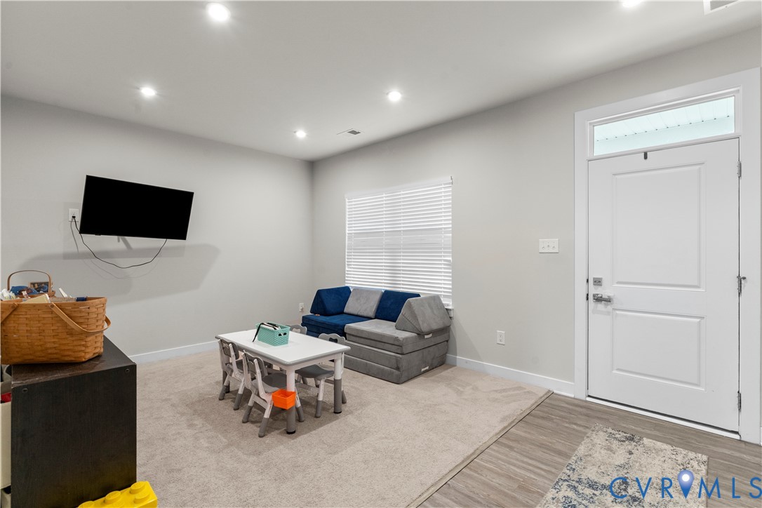 Recessed lighting, light gray wall paint, carpeting, a window with blinds, and a white door with transom window