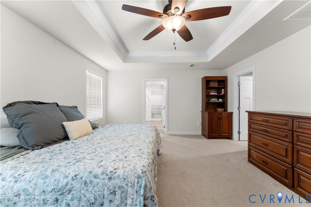 Tray ceiling with central ceiling fan, window with blinds, and neutral carpet flooring