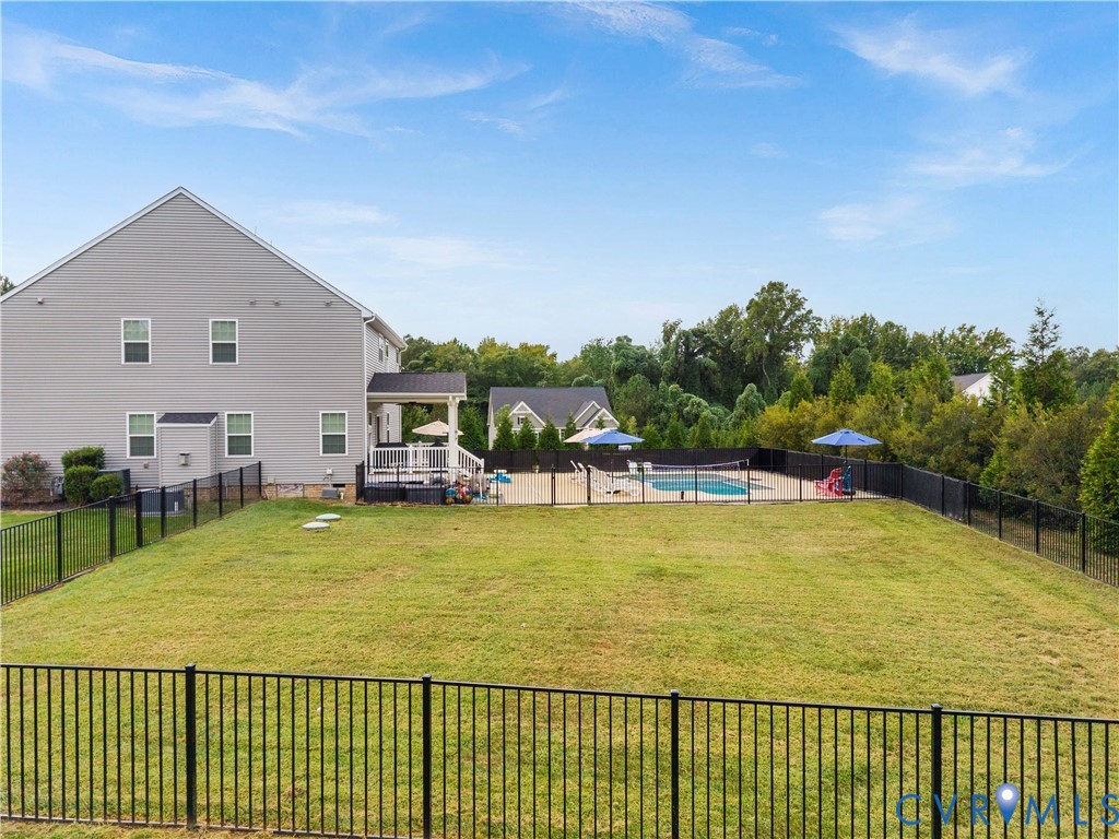 Expansive backyard featuring a fenced-in swimming pool, a covered deck, and a gray siding exterior