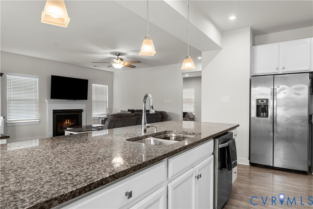 Kitchen island with stone-finish countertop, stainless steel sink with a high-arc faucet, white cabinetry, and recessed lighting
