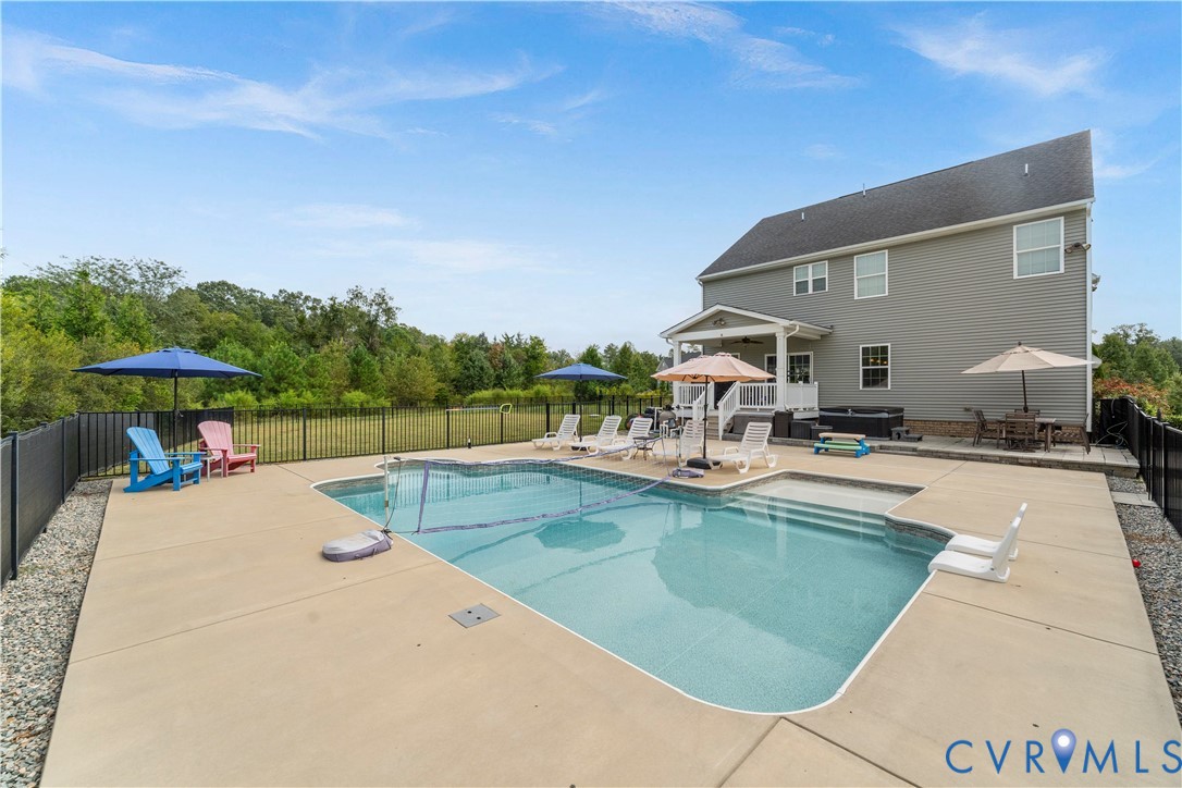 Swimming pool with integrated steps, concrete patio, rear exterior with covered porch, hot tub, and black metal fencing