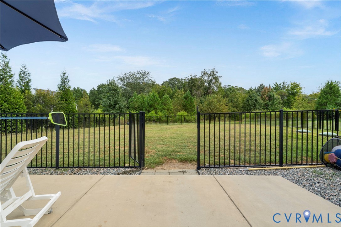 Expansive patio with concrete slab and gravel border, featuring a black metal fence with a double gate opening to a grassy area
