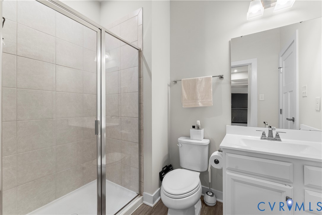 Shower enclosure with glass door, tiled shower surround, single vanity with integrated sink, chrome faucet, and wood-finish flooring
