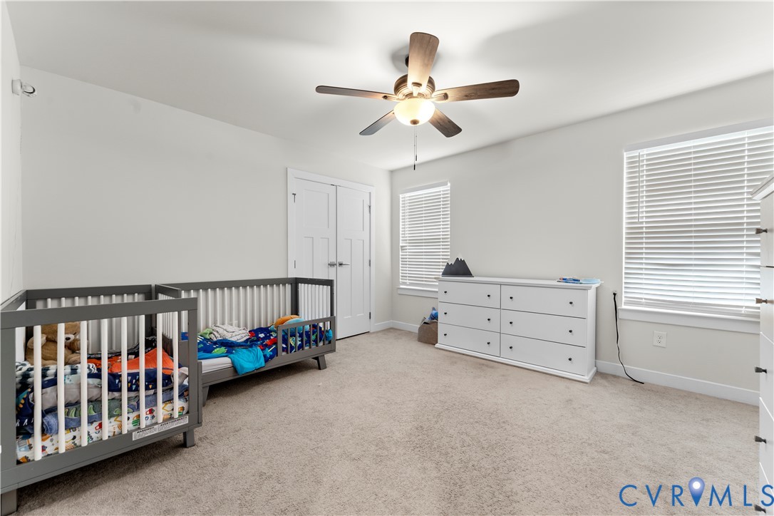 Carpeted room with white walls, a ceiling fan with light fixture, and two windows with blinds