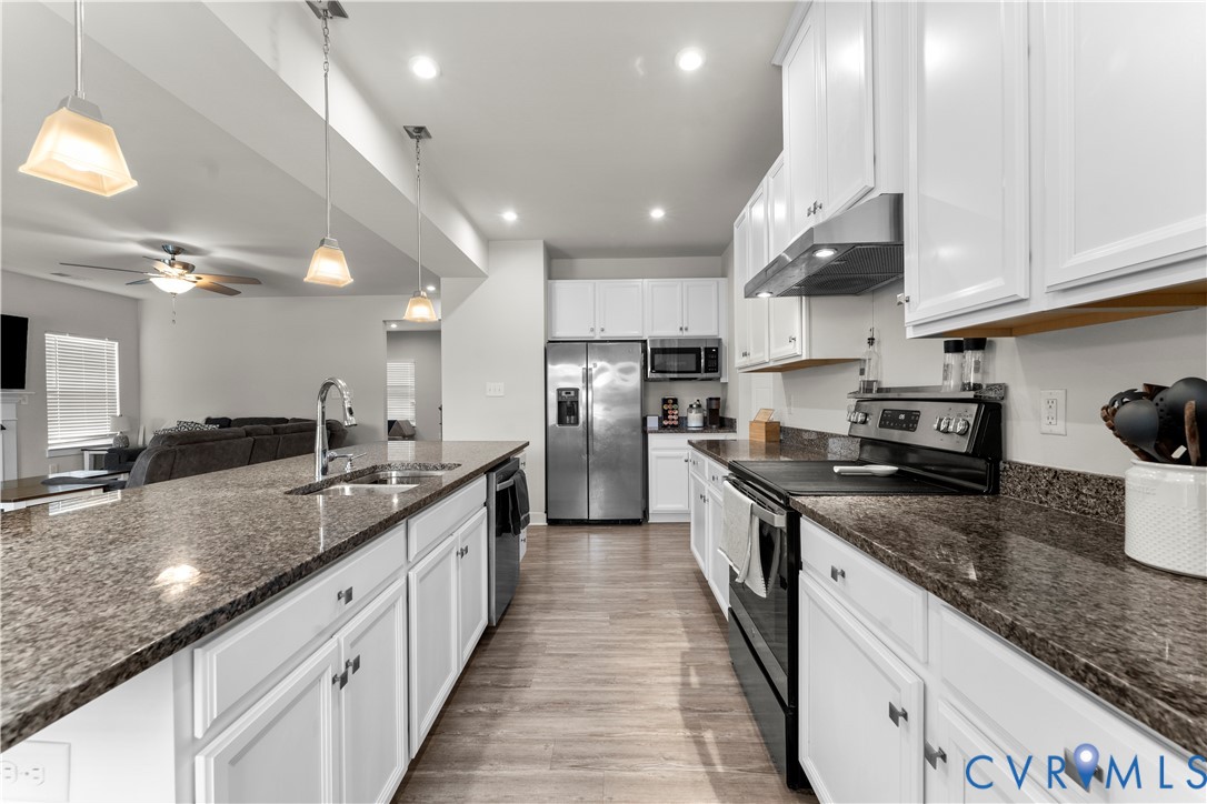 Kitchen featuring white cabinetry, dark speckled countertops, stainless steel appliances, and wood-finish flooring