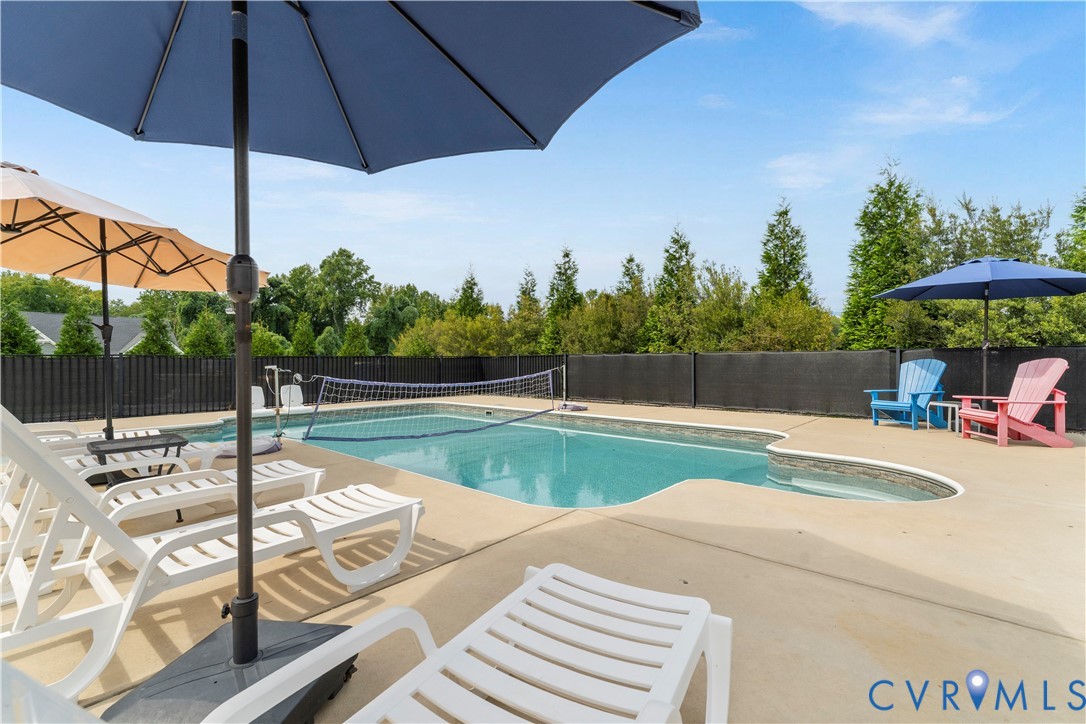 Swimming pool with integrated spa and concrete surround, privacy fencing, and mature perimeter trees