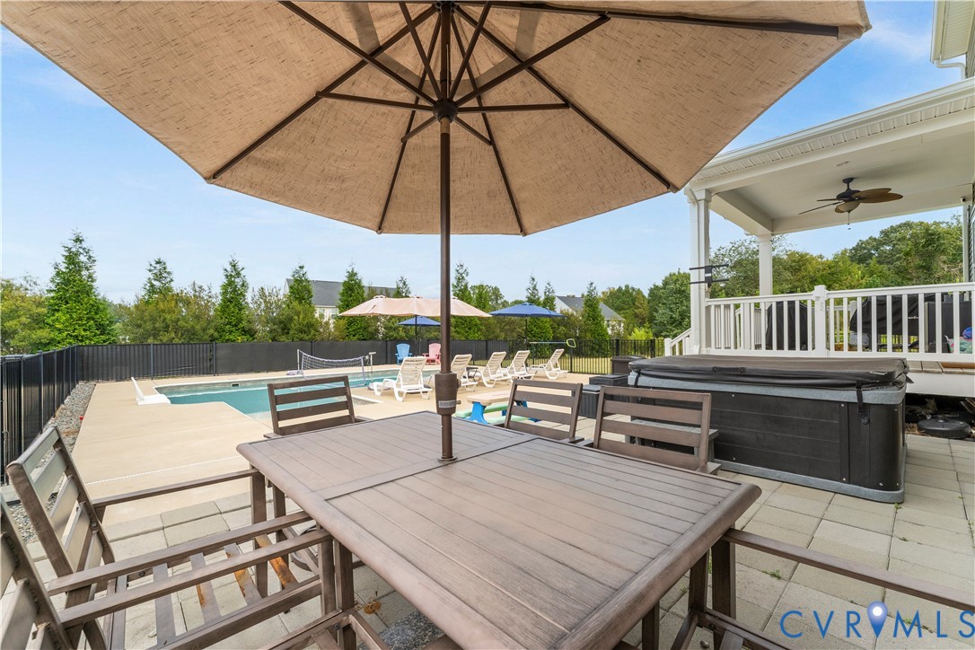 Patio with paver flooring, shaded by an umbrella, featuring a built-in spa, a swimming pool, and a covered porch with a ceiling fan