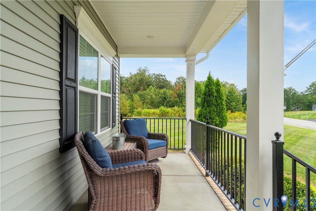 Covered front porch with concrete flooring, white columns, black railings, and light-colored siding