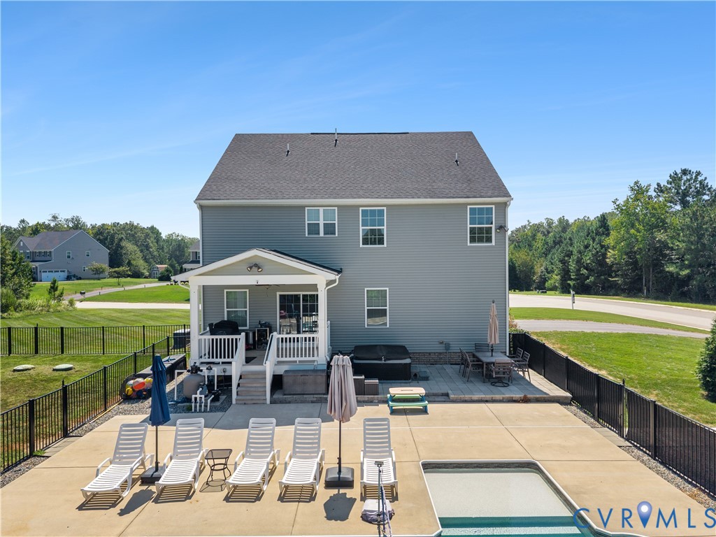 Expansive rear exterior featuring a covered porch, outdoor patio, in-ground pool, and a fenced yard