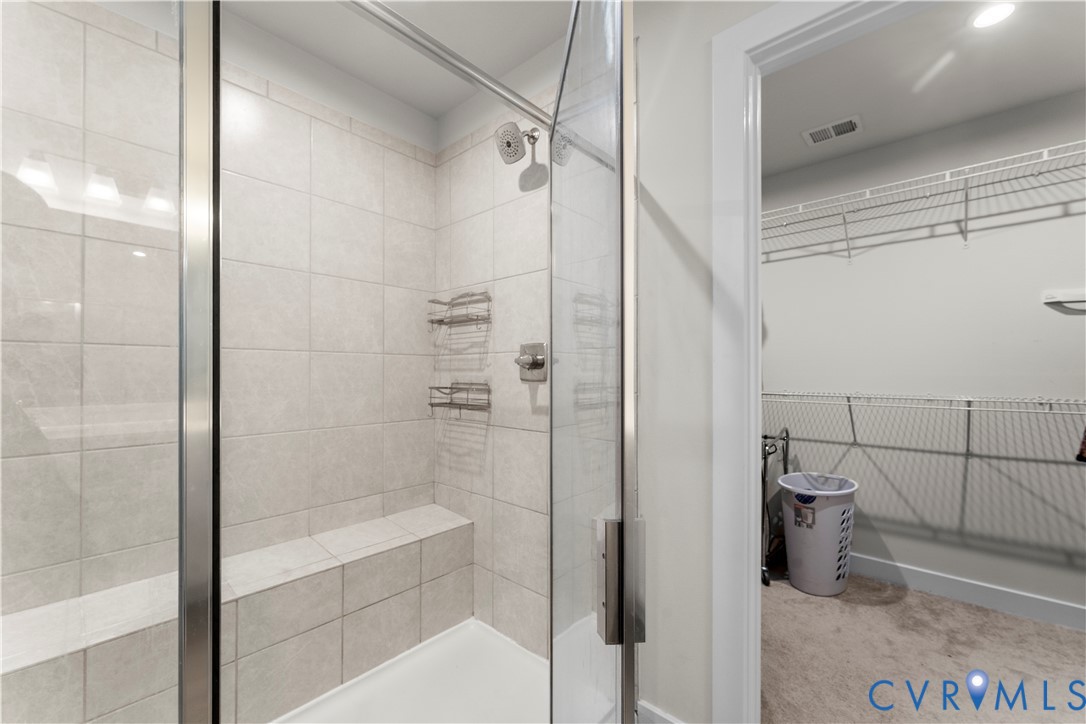 Shower with a glass enclosure, tile surround, built-in bench, and a brushed nickel showerhead