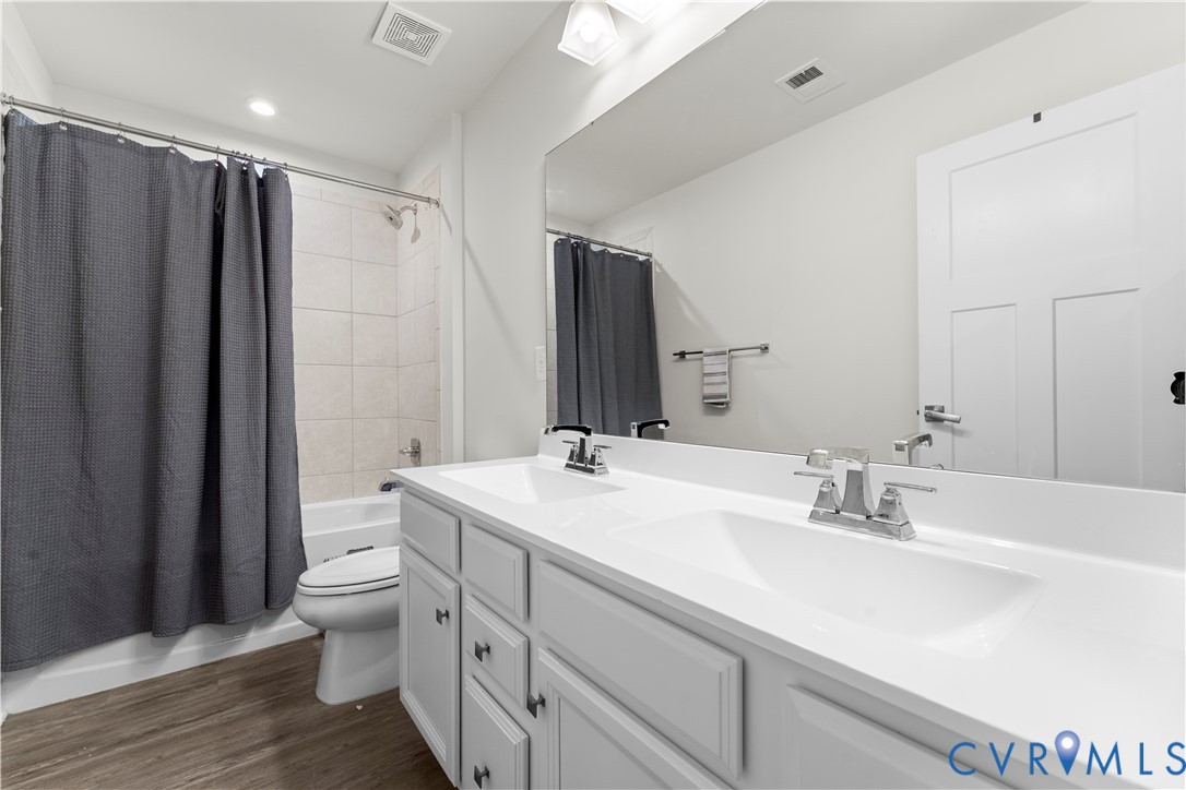 Dual vanity with integrated sinks, wood-finish flooring, white cabinetry, and a full-width mirror
