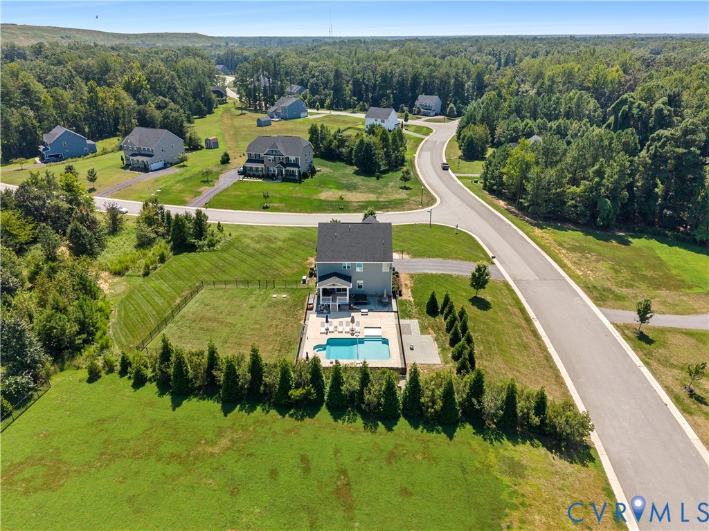 In-ground swimming pool with surrounding hardscape, privacy fencing, and mature landscaping