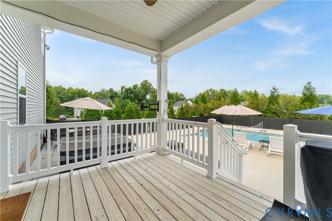 Covered deck with white railing overlooking a swimming pool, hot tub, and surrounding trees