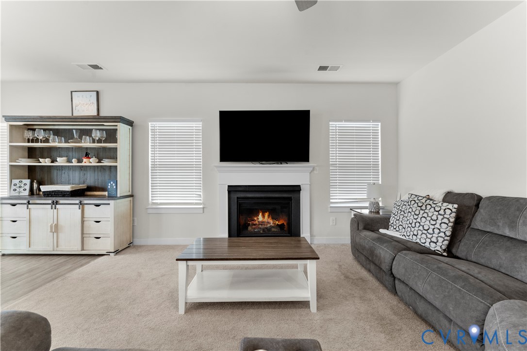 Living area featuring a fireplace with a white mantel, two windows with blinds, and a built-in cabinetry unit with open shelving and lower storage
