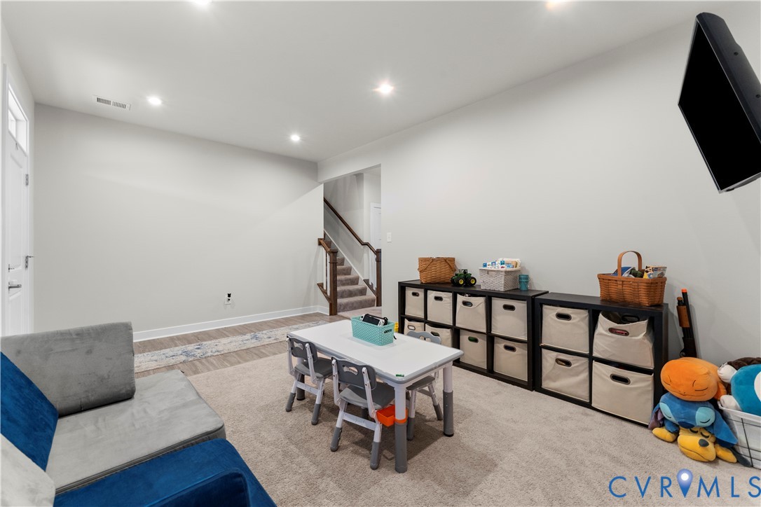 Recessed lighting illuminates the open area, featuring carpet flooring and wood-finish flooring