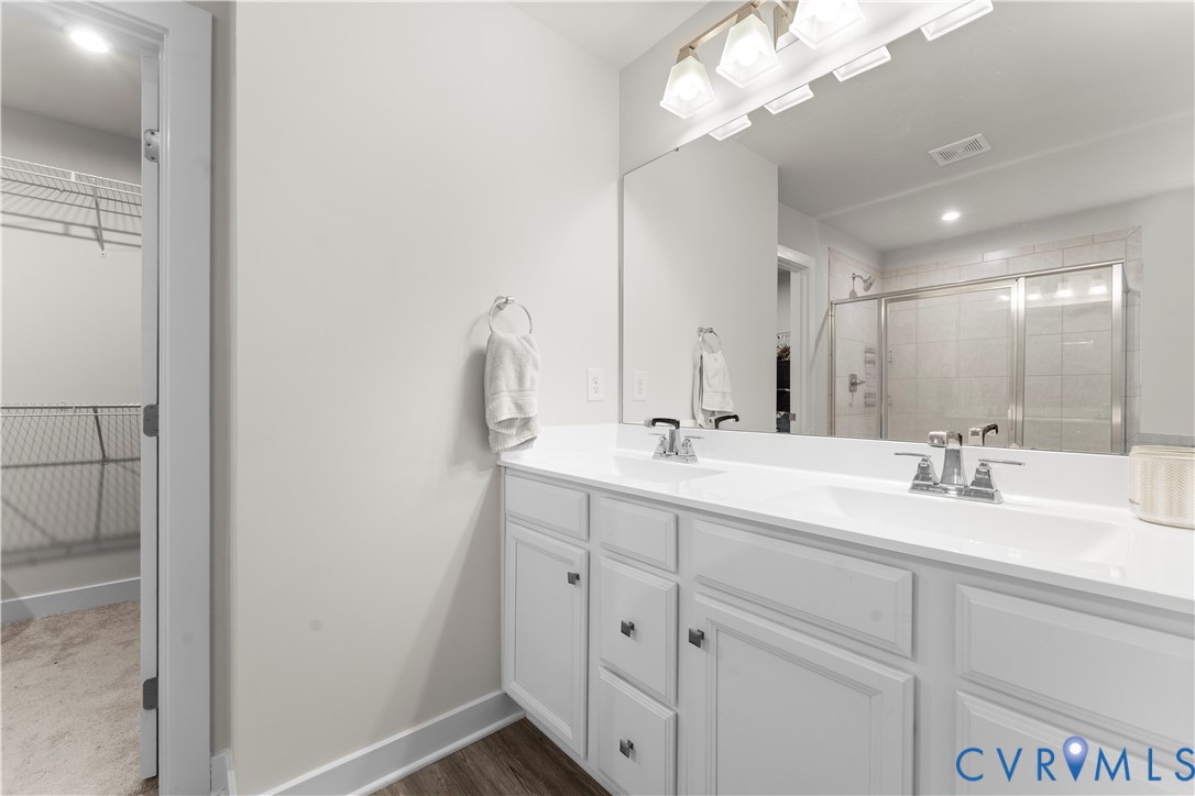 Double vanity with white cabinetry and integrated sinks, extensive mirror, and a walk-in shower with subway tile