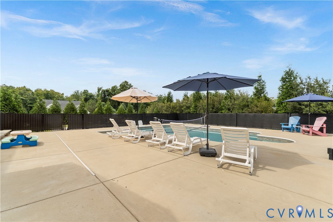 Outdoor swimming pool with a concrete surround, privacy fencing, and mature perimeter trees