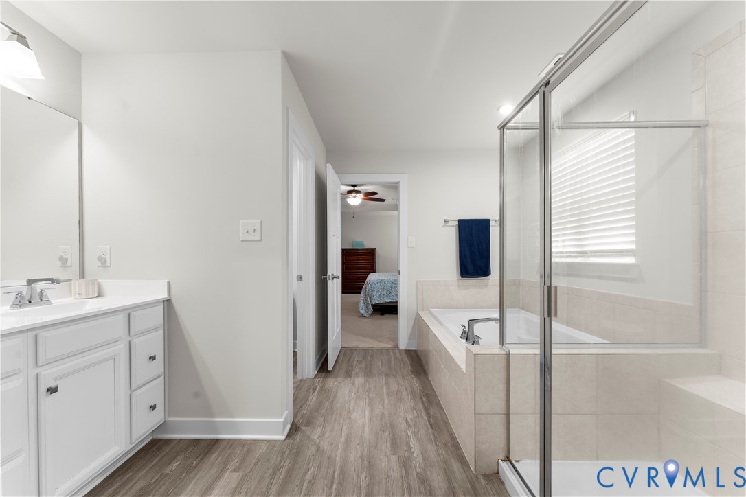 Bathroom featuring a single vanity with storage, a large soaking tub, a separate glass-enclosed shower, and wood-finish flooring