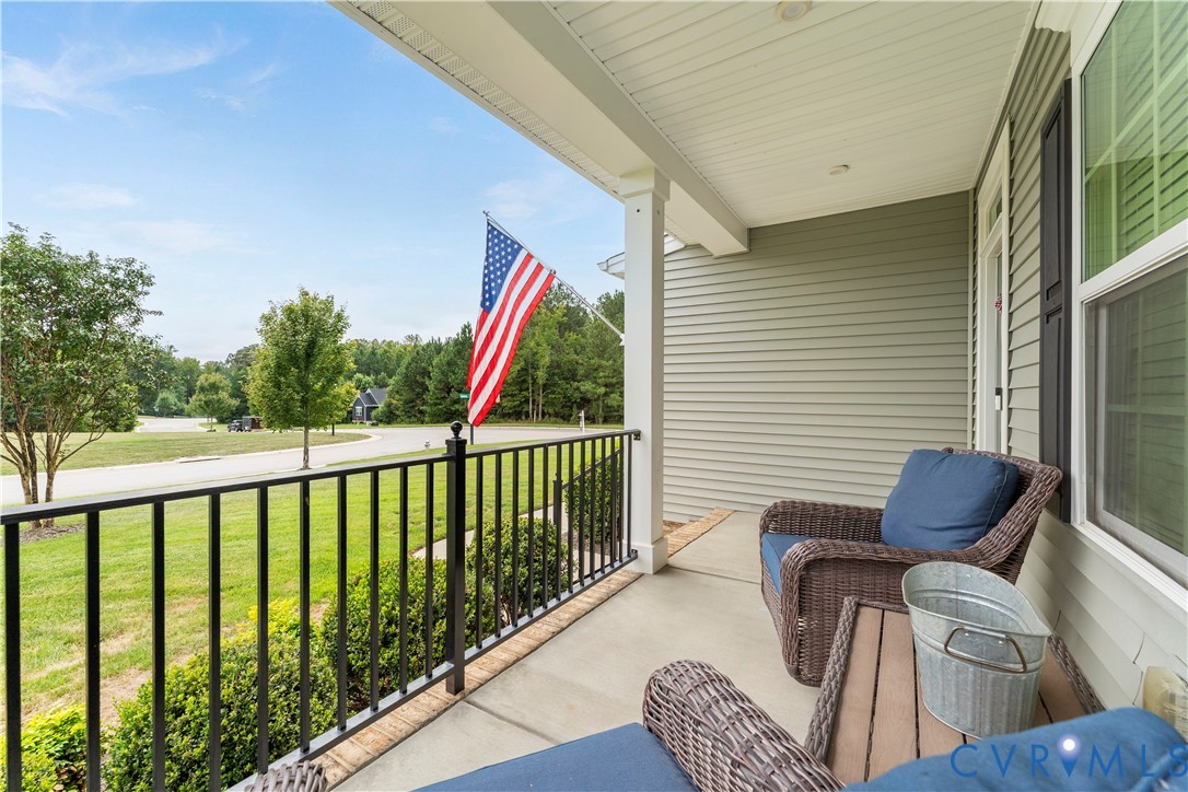 Covered front porch with concrete flooring, white columns, black railing, and siding exterior