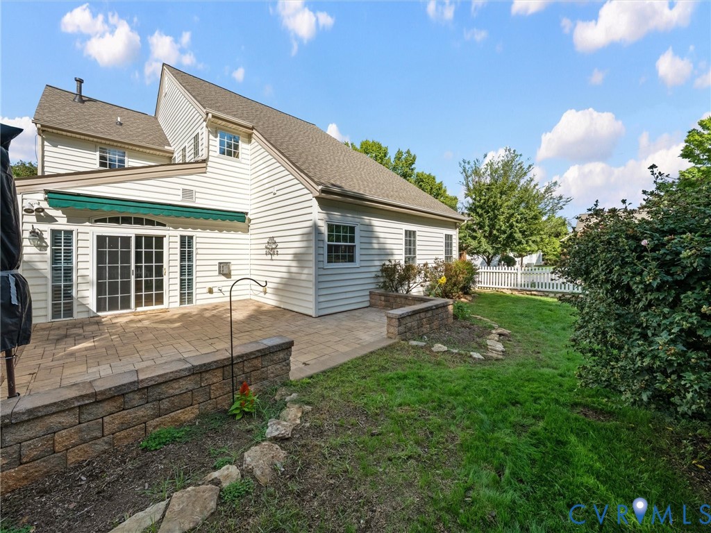 Paved patio with decorative retaining wall, awning, sliding glass doors, and white picket fencing