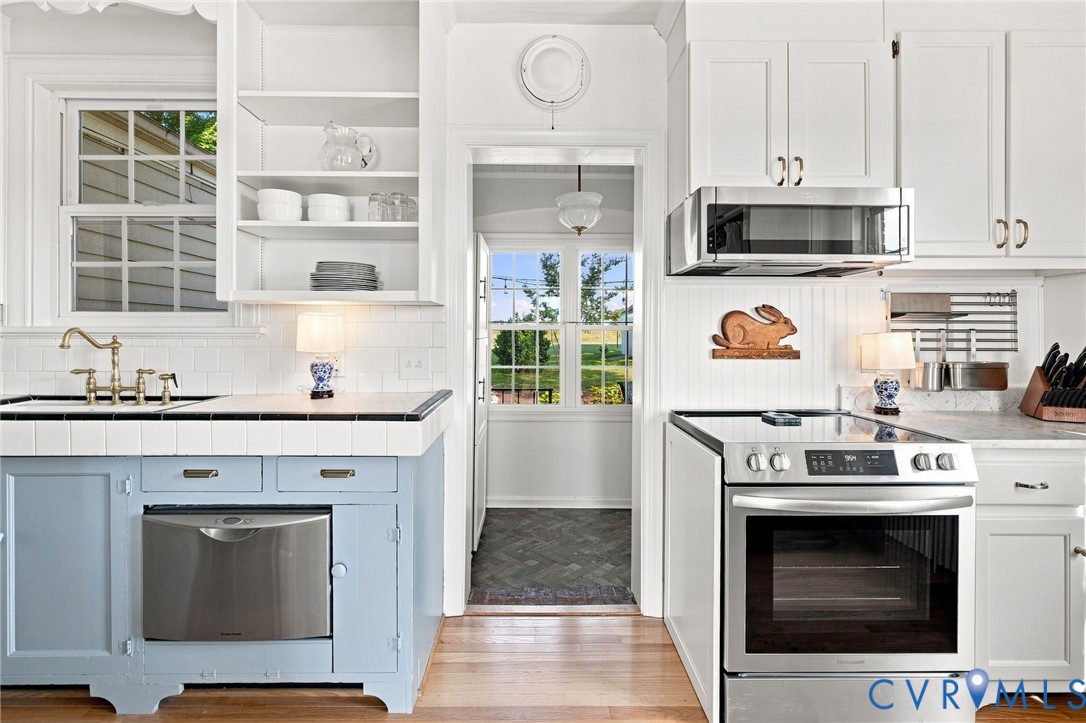White cabinetry with gold-tone hardware, stainless steel appliances, and wood-finish flooring