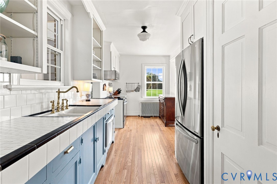 Kitchen featuring a stainless steel refrigerator, white subway tile backsplash, wood-finish flooring, and white cabinetry
