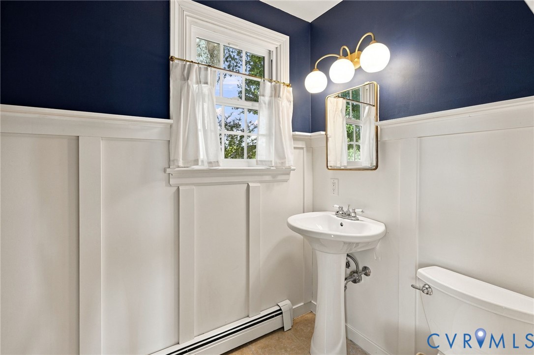 Pedestal sink with chrome faucet, board and batten wainscoting, wall-mounted mirror, and a three-light vanity fixture