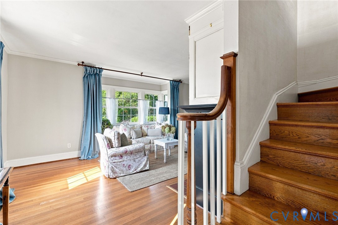 Hardwood flooring, painted walls, white crown molding, bay window, and a wood staircase with white risers Hardwood flooring, painted walls, white crown molding, bay window, and a wood staircase with white risers