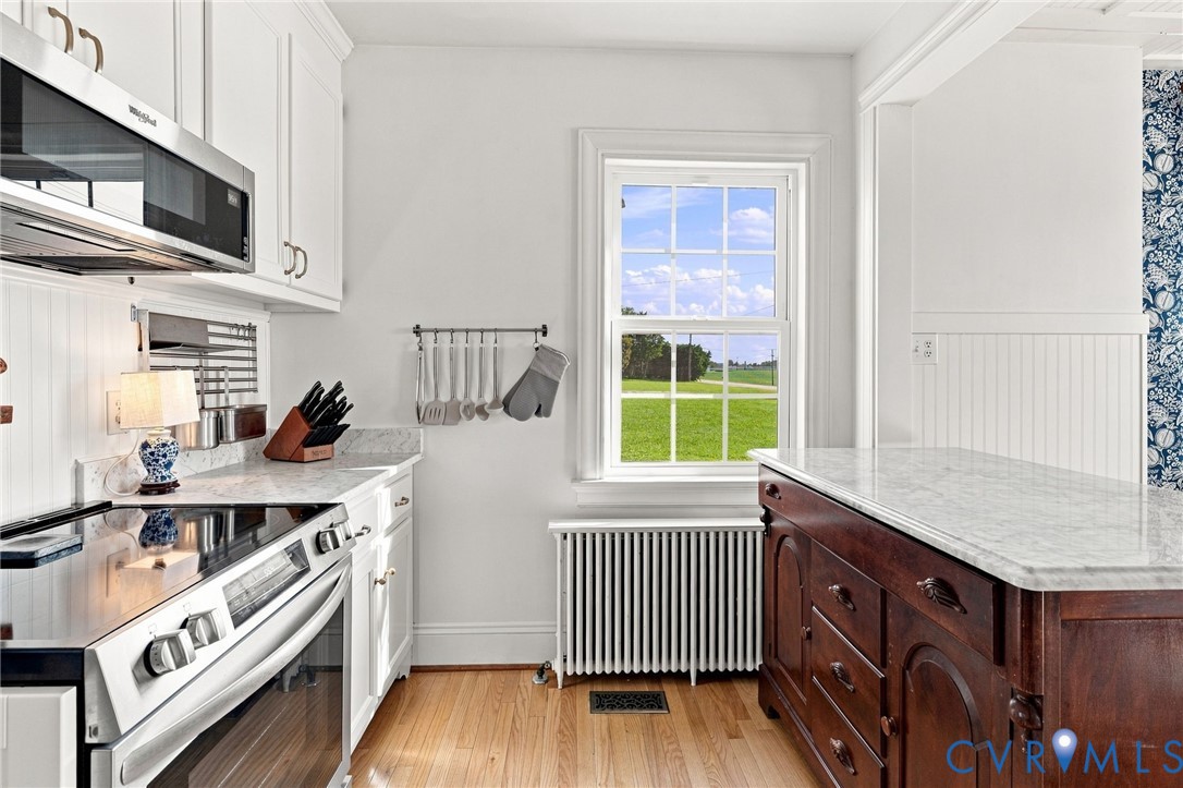 White cabinetry, stainless steel appliances, stone countertops, wood-finish flooring, and a window with a green landscape