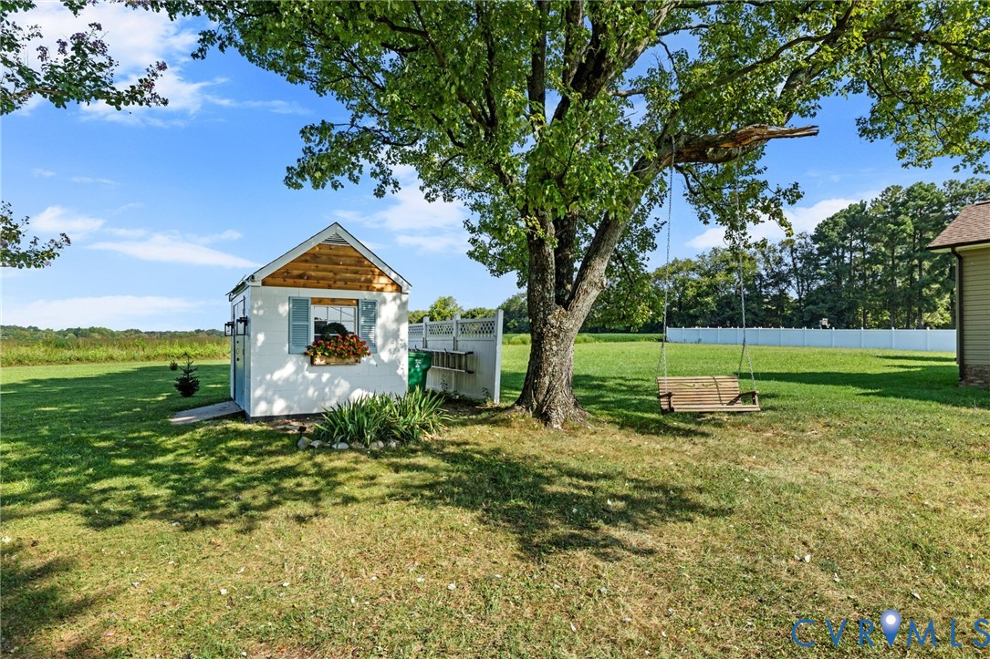 Detached storage shed with wood siding and shutters, mature tree, and expansive lawn
