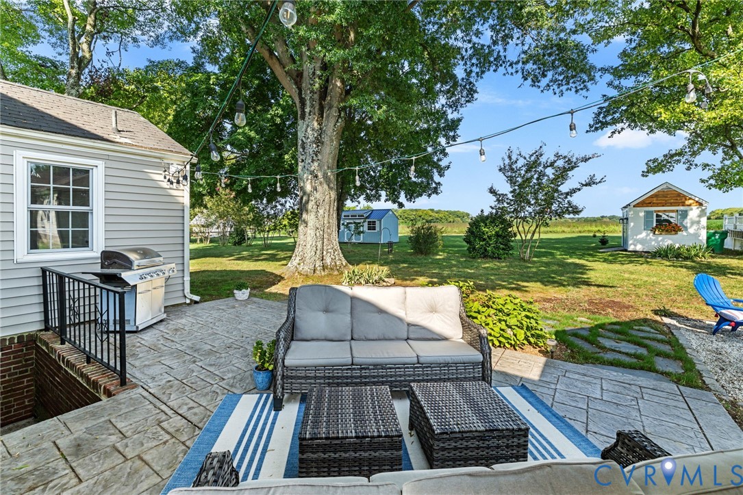 Expansive backyard featuring stone patio, string lighting, mature trees, and a detached shed