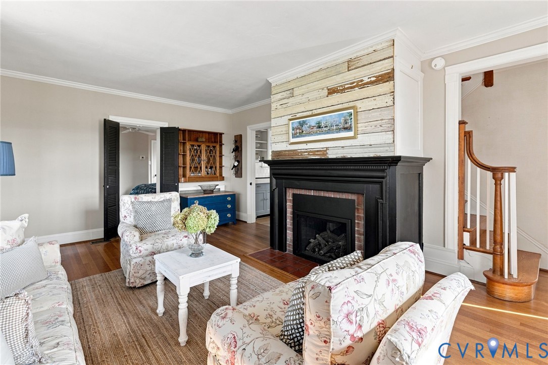 Hardwood flooring, fireplace with black mantel and brick surround, shiplap accent wall, built-in cabinetry, and a wood staircase with white balusters Hardwood flooring, fireplace with black mantel and brick surround, shiplap accent wall, built-in cabinetry, and a wood staircase with white balusters