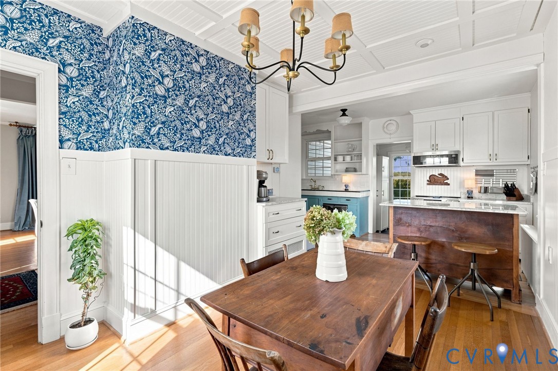 Hardwood flooring, coffered ceiling, white wainscoting, and an open-concept kitchen with white cabinetry and a wood-finish island