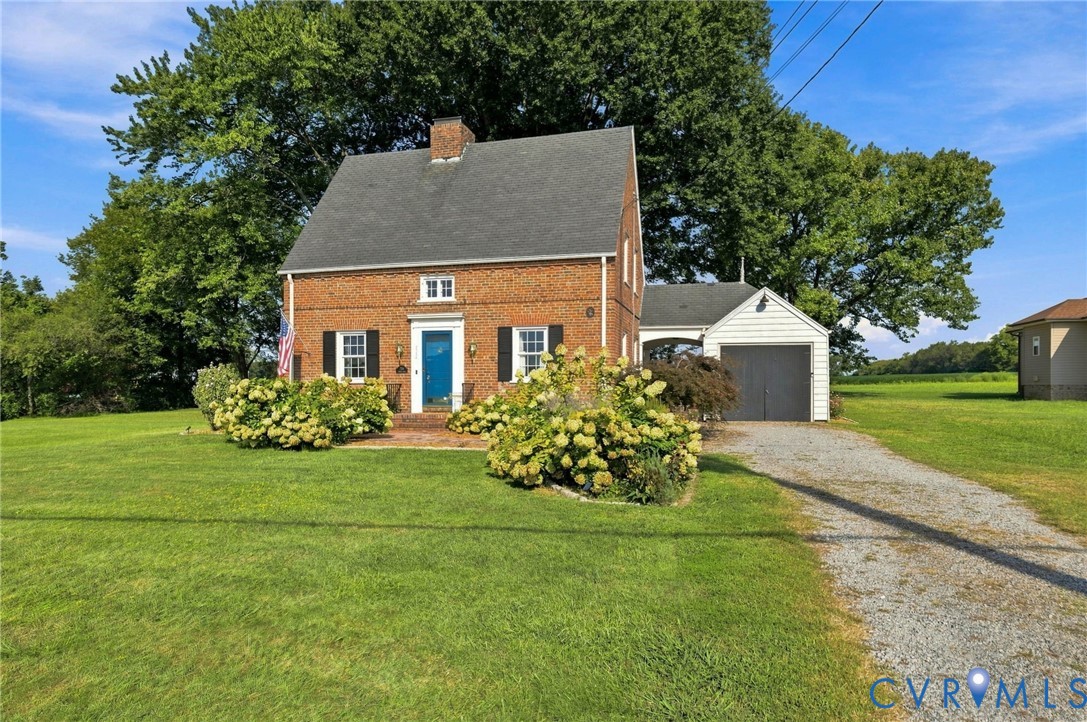 Brick exterior with dark shutters, a blue entry door, and a gravel driveway