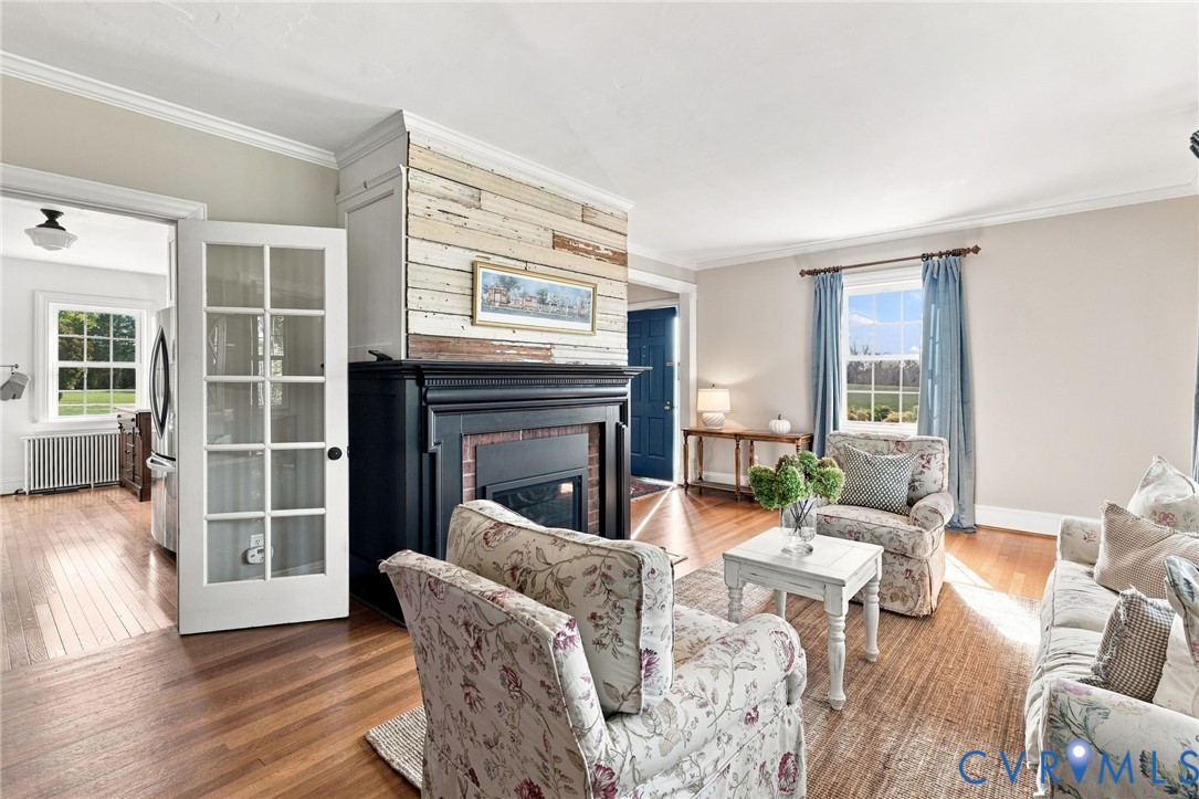 Hardwood flooring throughout, a fireplace with a black mantel and brick surround, crown molding, and a paneled glass door Hardwood flooring throughout, a fireplace with a black mantel and brick surround, crown molding, and a paneled glass door