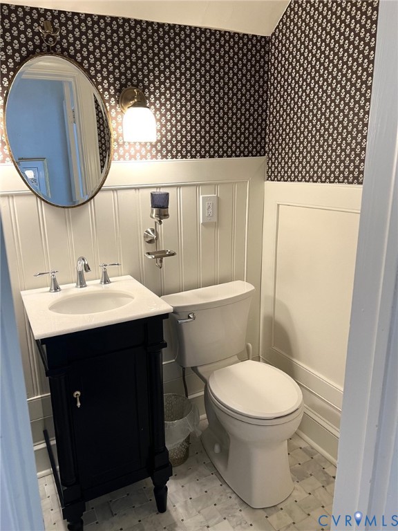 Black vanity with a white countertop and undermount sink, patterned wallpaper, beadboard wainscoting, and mosaic tile flooring Black vanity with a white countertop and undermount sink, patterned wallpaper, beadboard wainscoting, and mosaic tile flooring