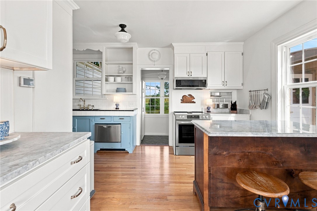 Hardwood flooring, white cabinetry, a kitchen island with stone countertop, stainless steel appliances, and a built-in dishwasher