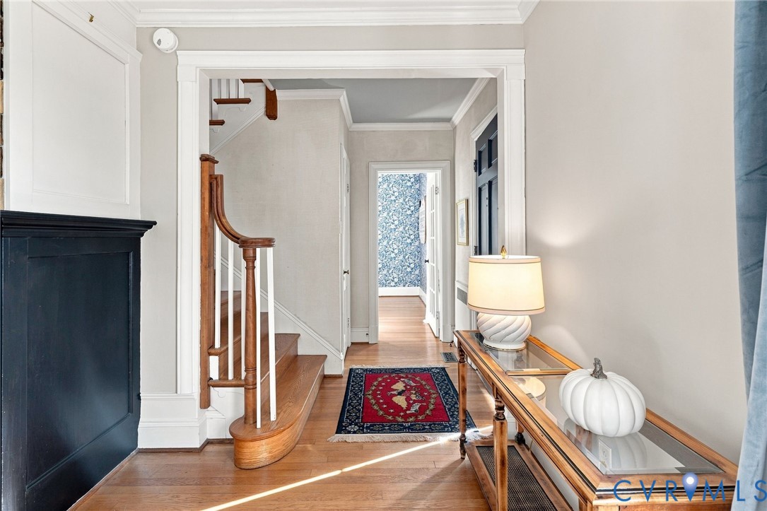 Hardwood flooring, staircase with wood handrail and white balusters, crown molding, and framed doorway Hardwood flooring, staircase with wood handrail and white balusters, crown molding, and framed doorway