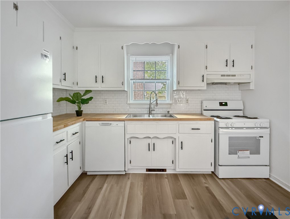 White cabinetry with matte black hardware, wood-finish countertops, subway tile backsplash, stainless steel sink, and wood-finish flooring White cabinetry with matte black hardware, wood-finish countertops, subway tile backsplash, stainless steel sink, and wood-finish flooring