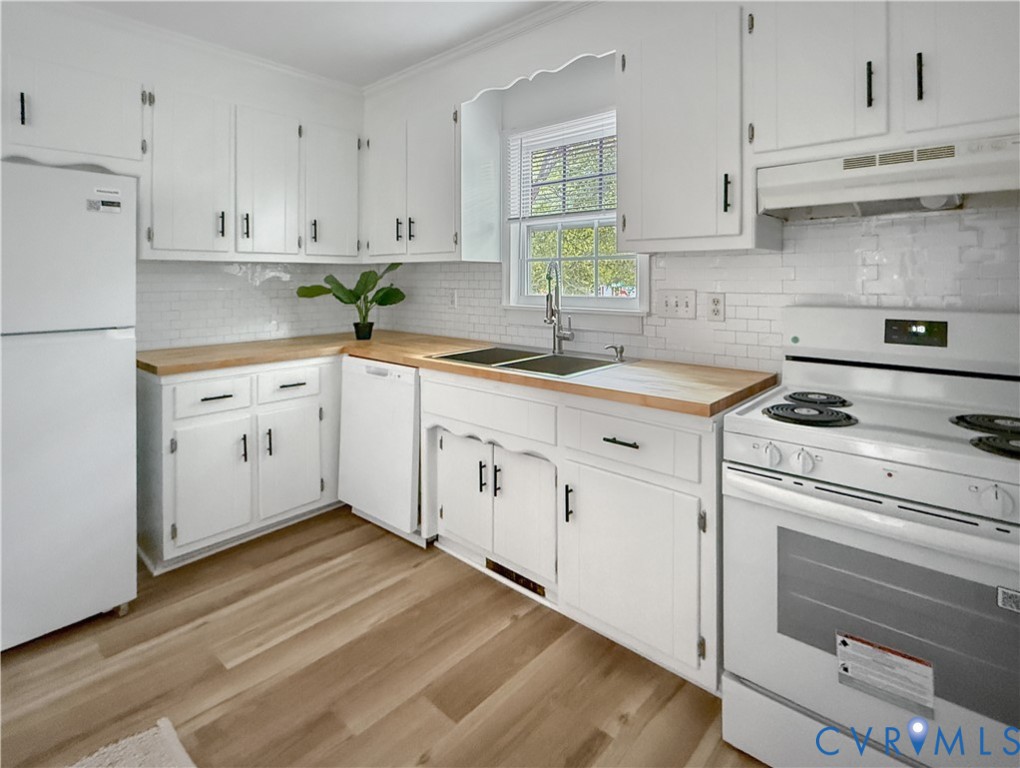 White cabinetry with matte black hardware, wood-finish countertops, white subway tile backsplash, and light wood-finish flooring