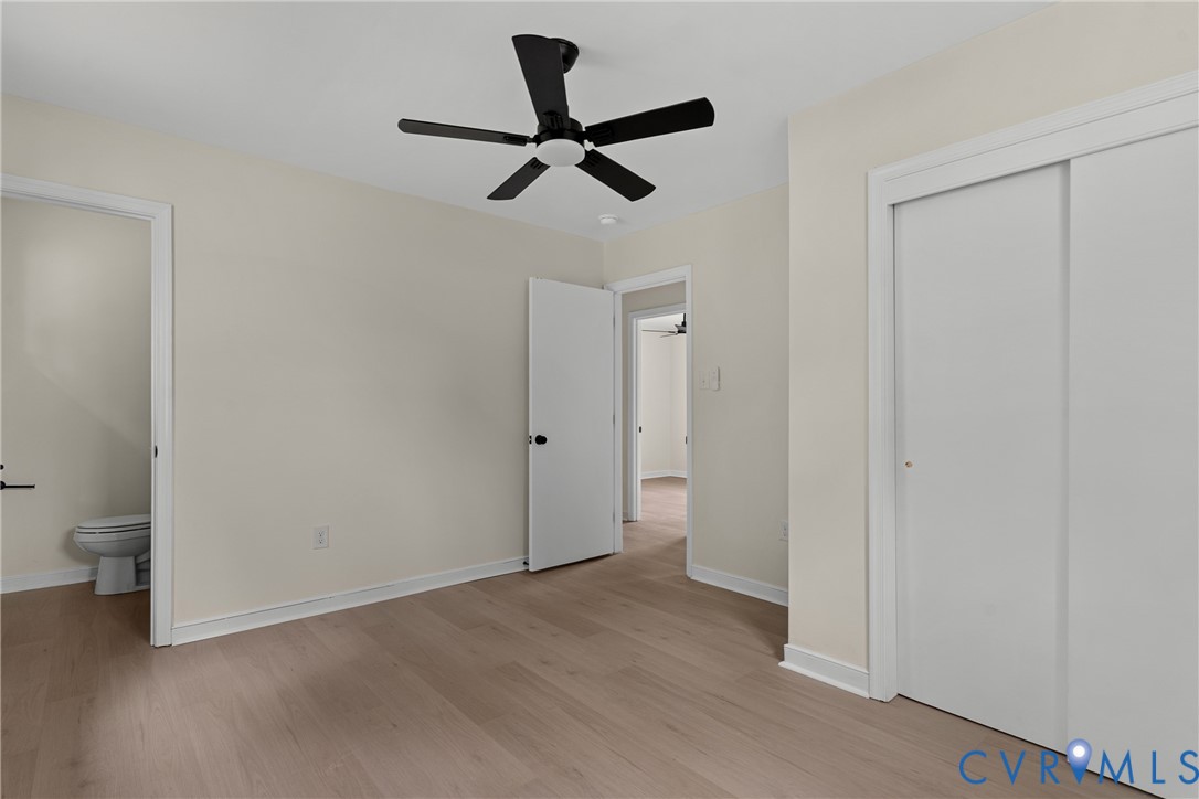 Interior room featuring light-toned walls, wood-finish flooring, and a black ceiling fan with integrated lighting