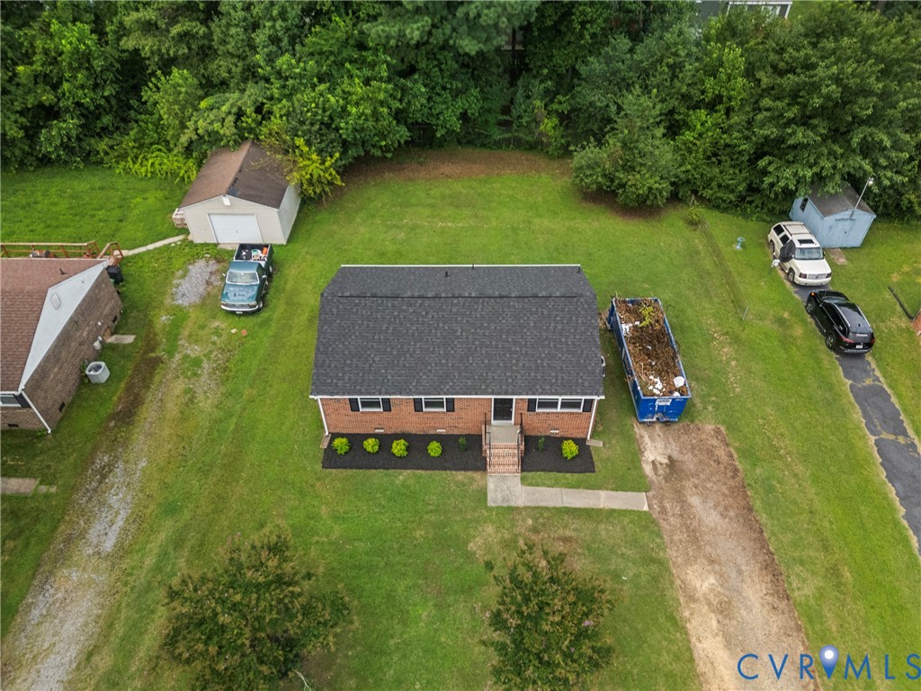 Brick facade home with a black shingle roof, featuring a concrete walkway, mature landscaping, and a detached storage shed