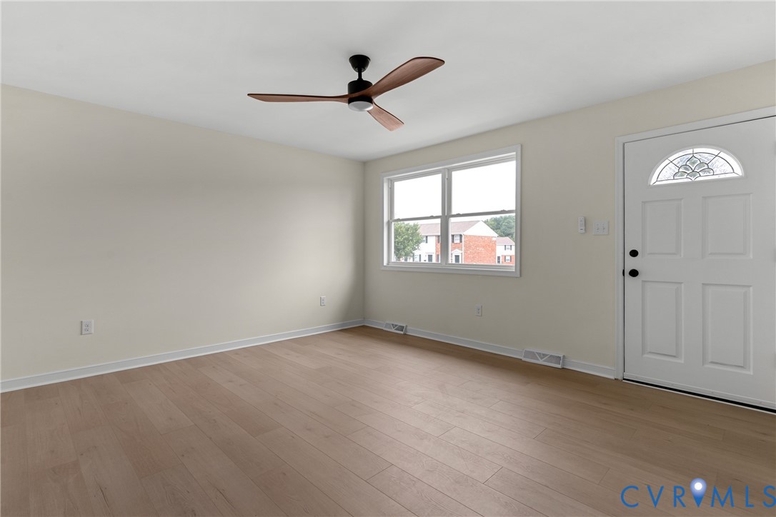 Bright living space featuring wood-finish flooring, a contemporary ceiling fan with wooden blades, and neutral painted walls