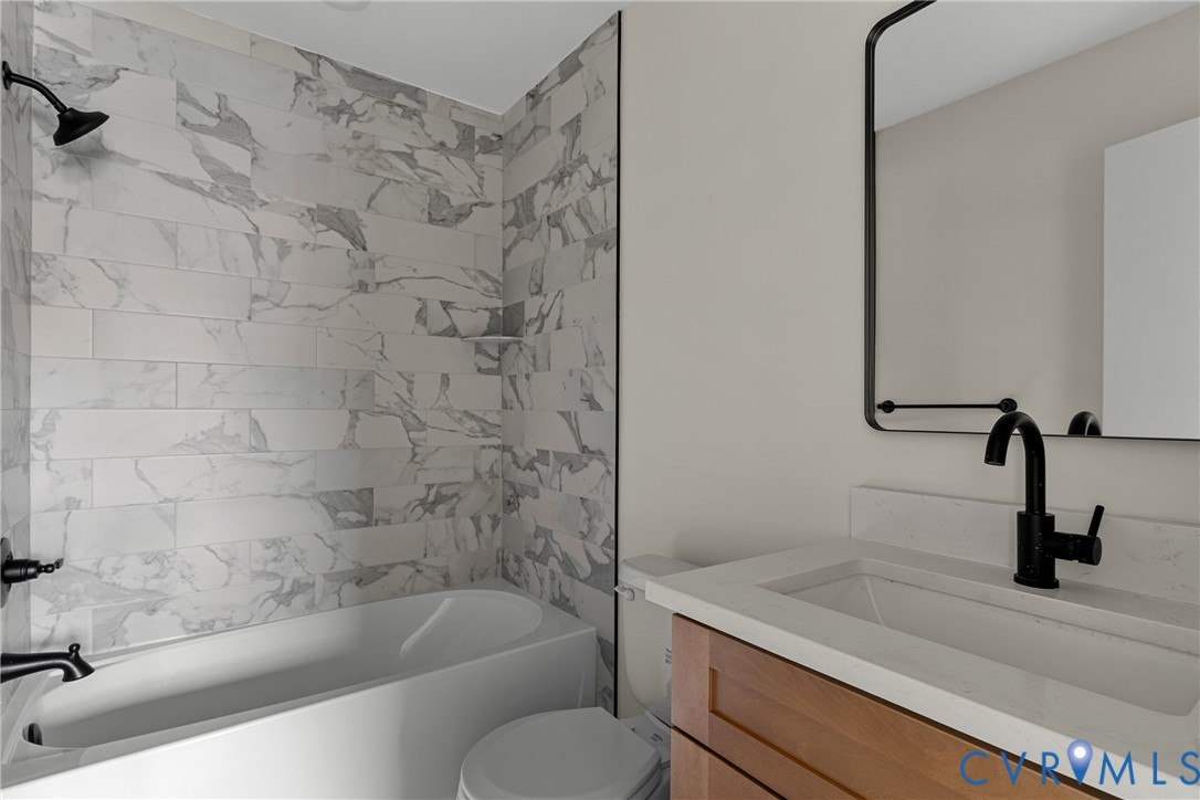Bathroom featuring a combined tub and shower with marble-look subway tile surround, matte black fixtures, a floating wood-finish vanity with an integrated sink, and a framed mirror