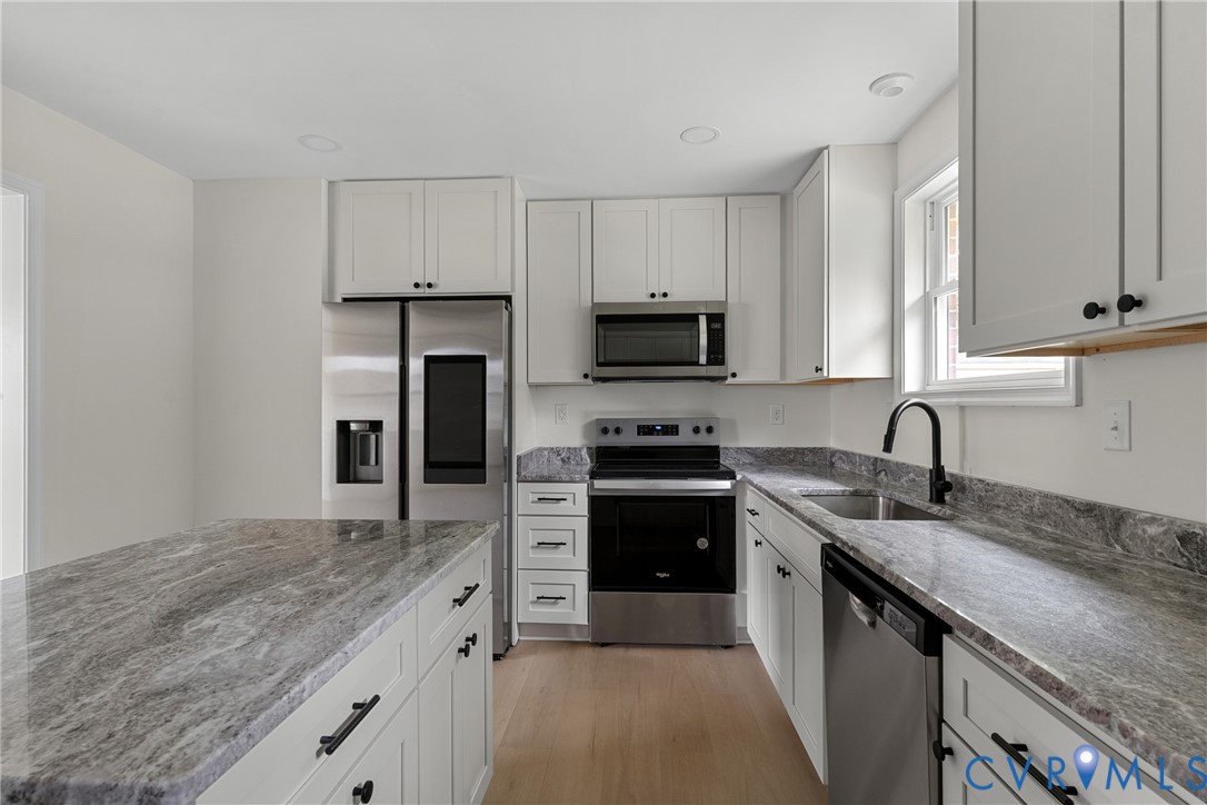 Kitchen featuring white cabinetry, gray patterned countertops, stainless steel appliances, and light wood-finish flooring