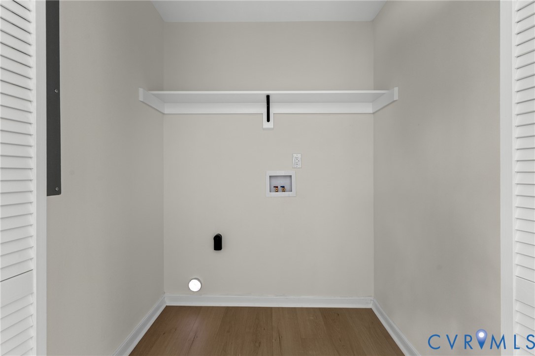 Dedicated utility space featuring wood-finish flooring, light neutral wall tones, a built-in storage shelf, and louvered doors