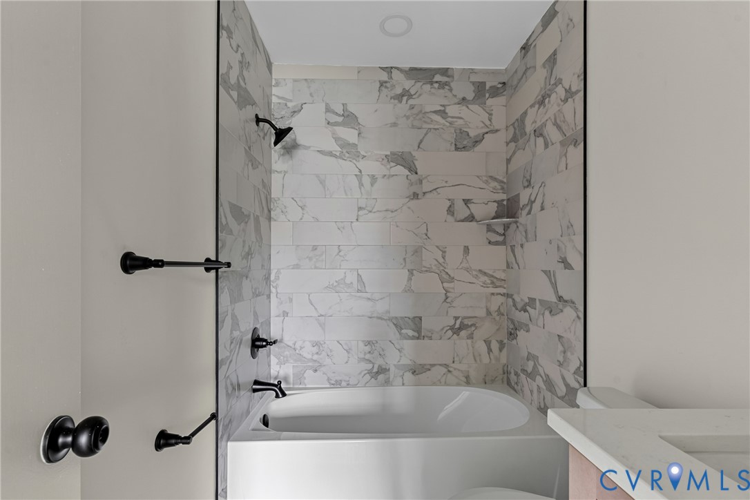 Bathtub and shower combination featuring marble-look tile surround and matte black fixtures