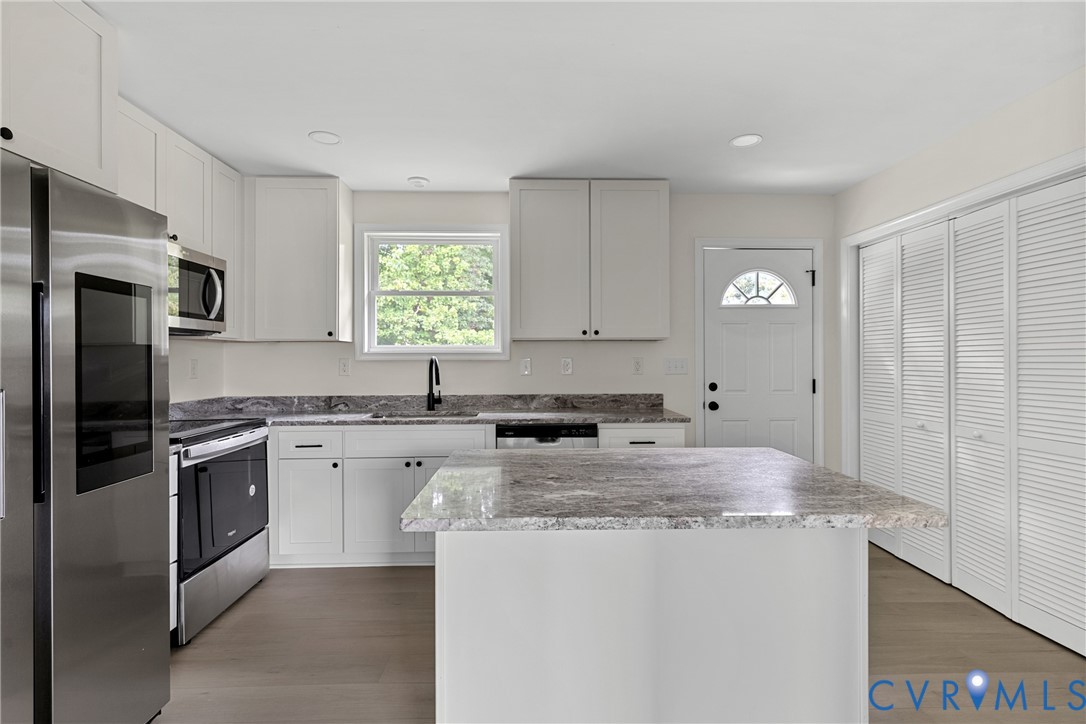 Modern kitchen featuring a central island with a stone countertop, white shaker-style cabinetry, and stainless steel appliances