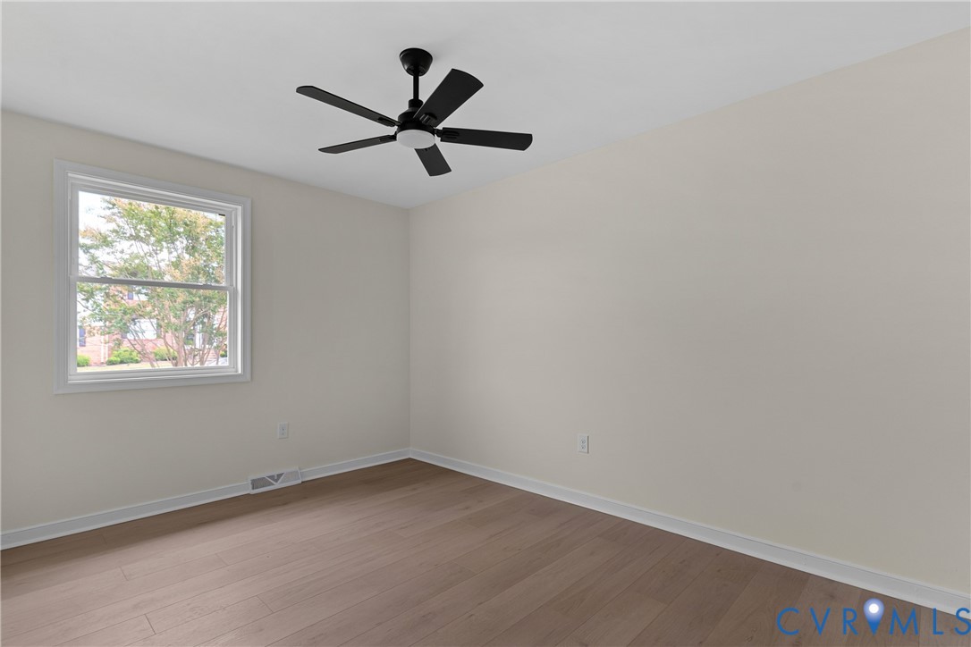 Room featuring wood-finish flooring, a white window frame, and a black ceiling fan with an integrated light